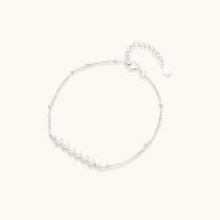 Delicate rhodium-plated silver chain bracelet with row of small baroque pearls centered on white background.