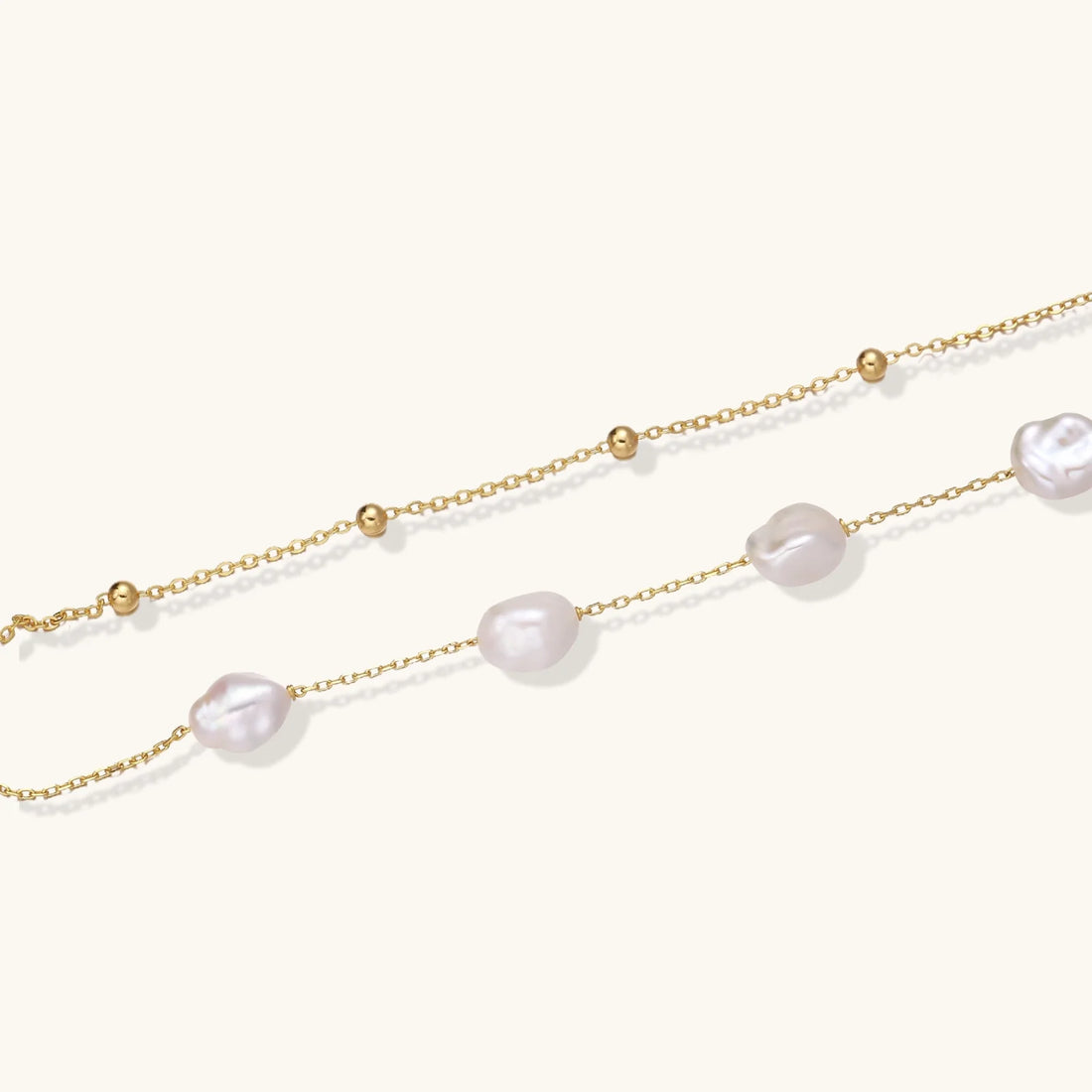 Double-strand gold bracelet with irregular baroque pearls and smooth freshwater pearls on cream background.