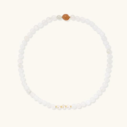 Three layered white beaded bracelets with carved orange agate lotus centerpiece and freshwater pearls on cream background.