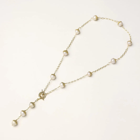 Gold-plated lariat necklace with baroque pearls and textured caps on cream background, showing adjustable Y-shaped design.