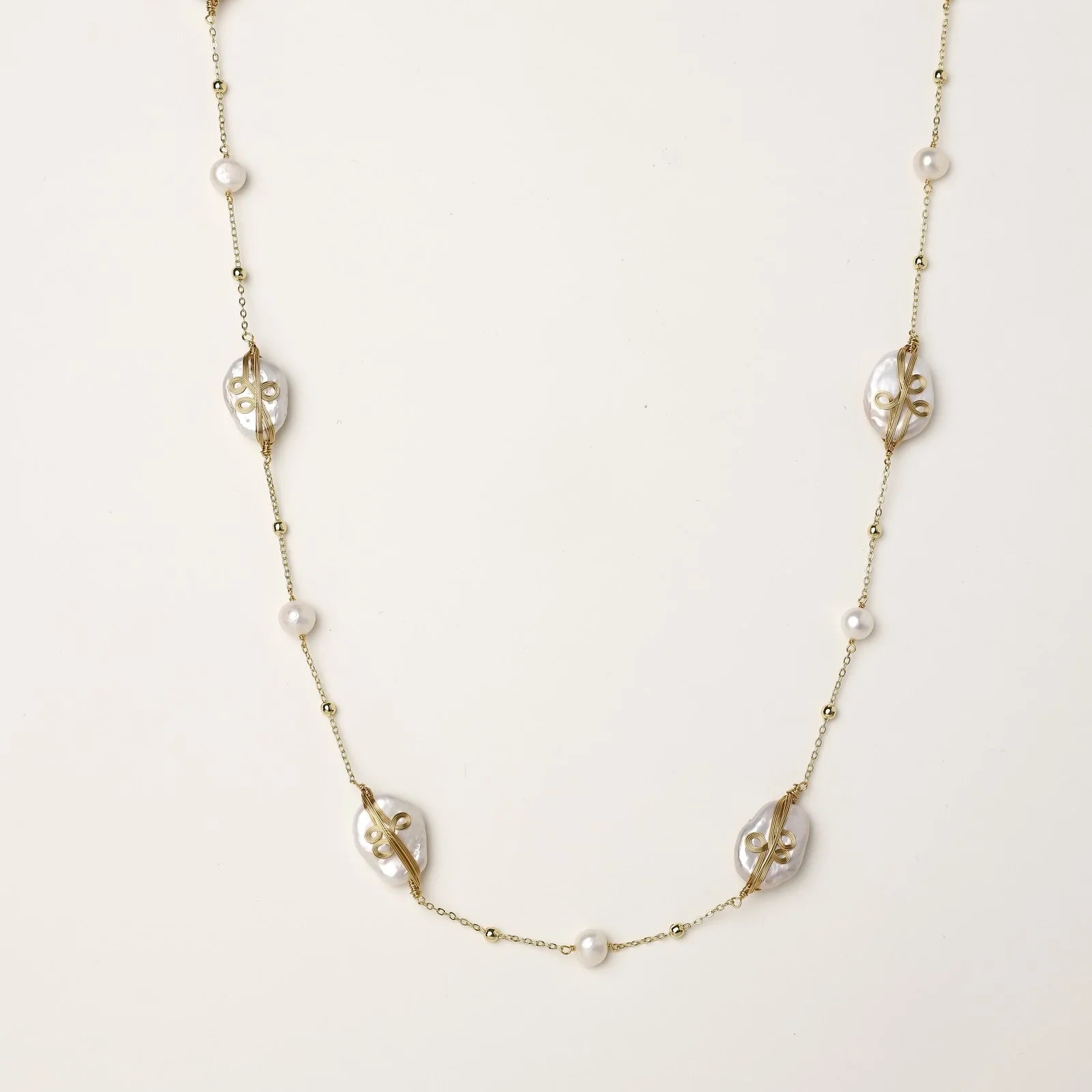 Long gold chain necklace with baroque pearls wrapped in leaf designs and small freshwater pearls spaced along the strand
