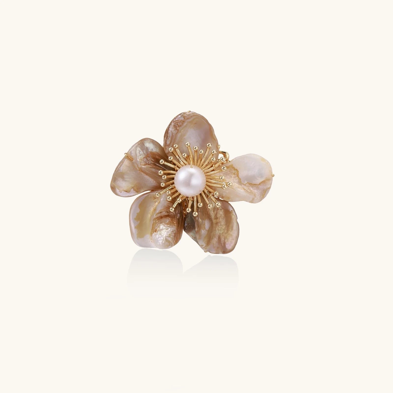 Flower-shaped brooch with iridescent shell petals, freshwater pearl center, and gold-plated radiating details.