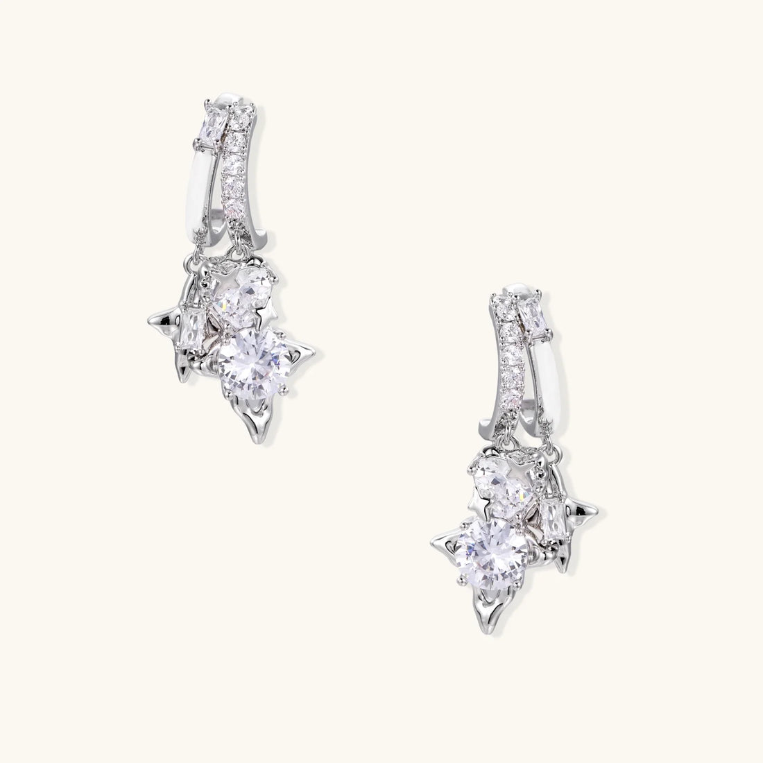 White gold-plated huggie earrings with geometric emerald-cut zirconia clusters in starburst formation on beige background
