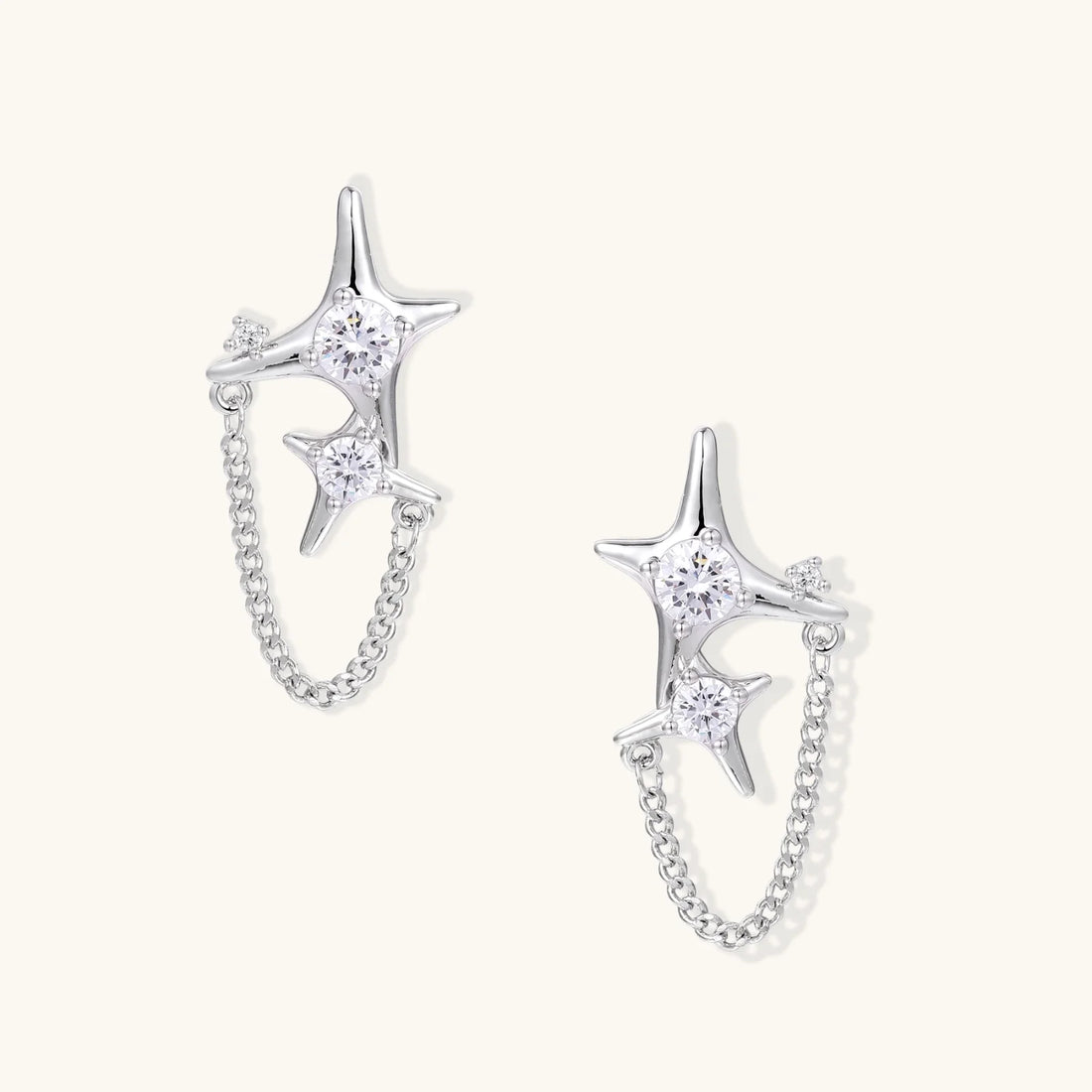 Silver star studs with crescent moon cutouts and zirconia stones connected by delicate chains on white background