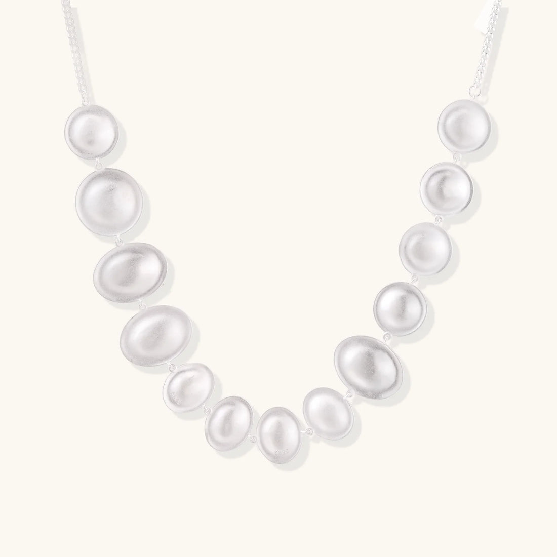 Graduated pearl-finish silver discs forming an organic bubble bib necklace on delicate chain against cream background.