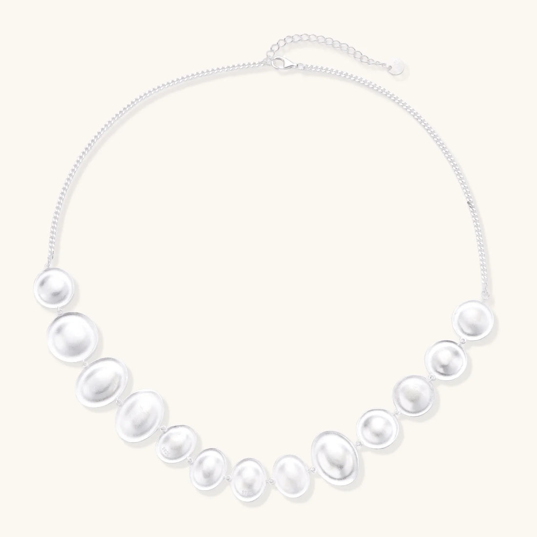 Graduated pearl-finish silver discs forming an organic bubble bib necklace on delicate chain against cream background.