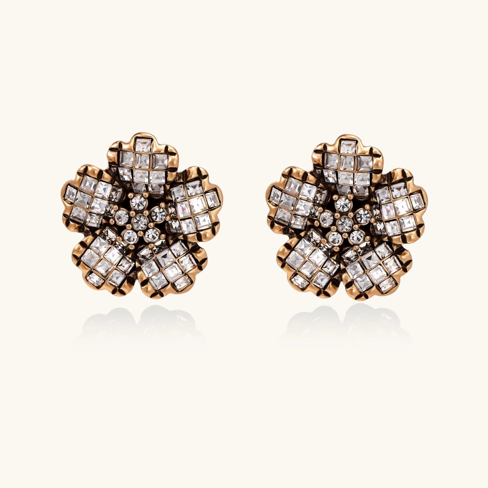 Gold-plated floral stud earrings with geometric zirconia crystals arranged in five-petal design on cream background