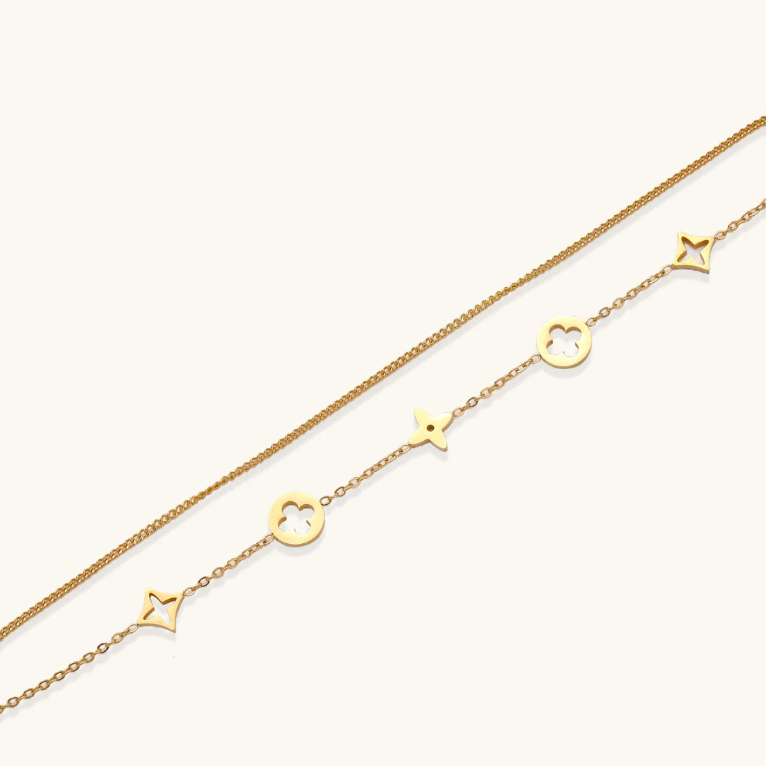 Double-layer gold-plated bracelet with quatrefoil and star charms on cream background, 18K gold finish.