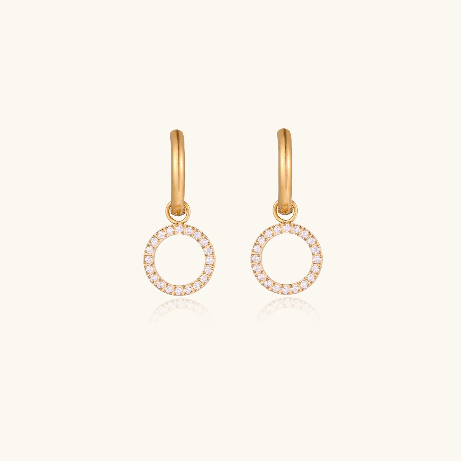 Gold-plated huggie hoop earrings with CZ-studded open circle charms on beige background