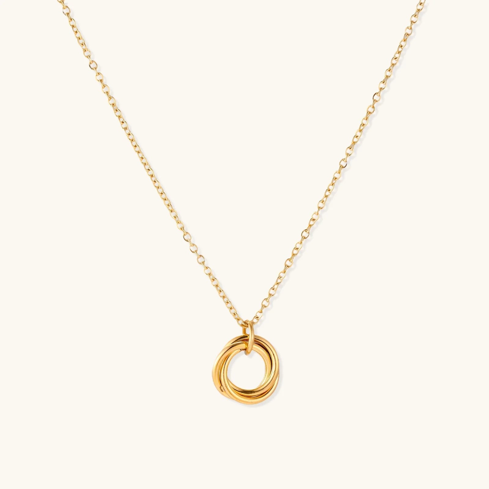 Delicate gold-plated necklace with three interlocking circle rings forming a minimalist knot pendant on cream background