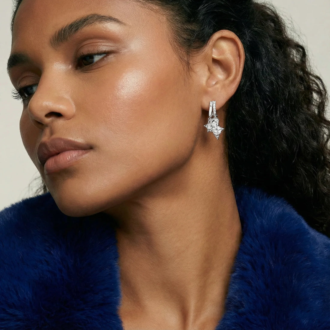 White gold-plated huggie earrings with geometric emerald-cut zirconia clusters in starburst formation on beige background