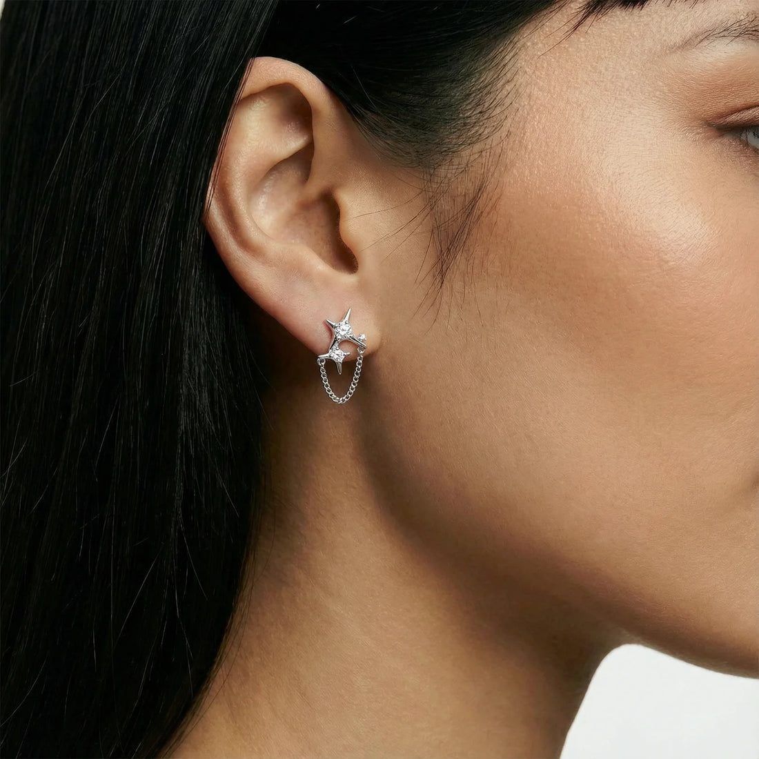 Silver star studs with crescent moon cutouts and zirconia stones connected by delicate chains on white background